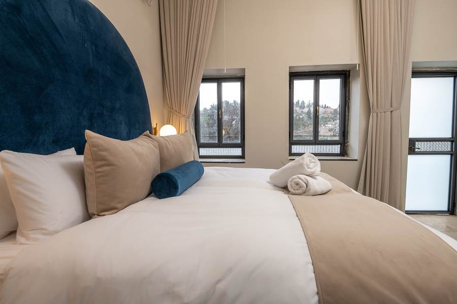 Bright suite bedroom with tall windows and hillside view